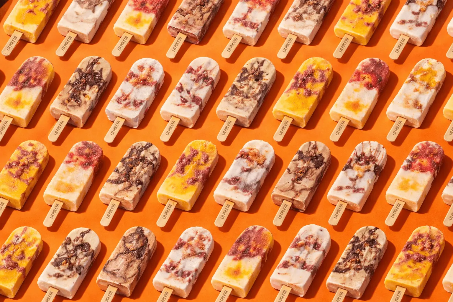 Rows of colorful LA PALETA paletas arranged on a vibrant orange background