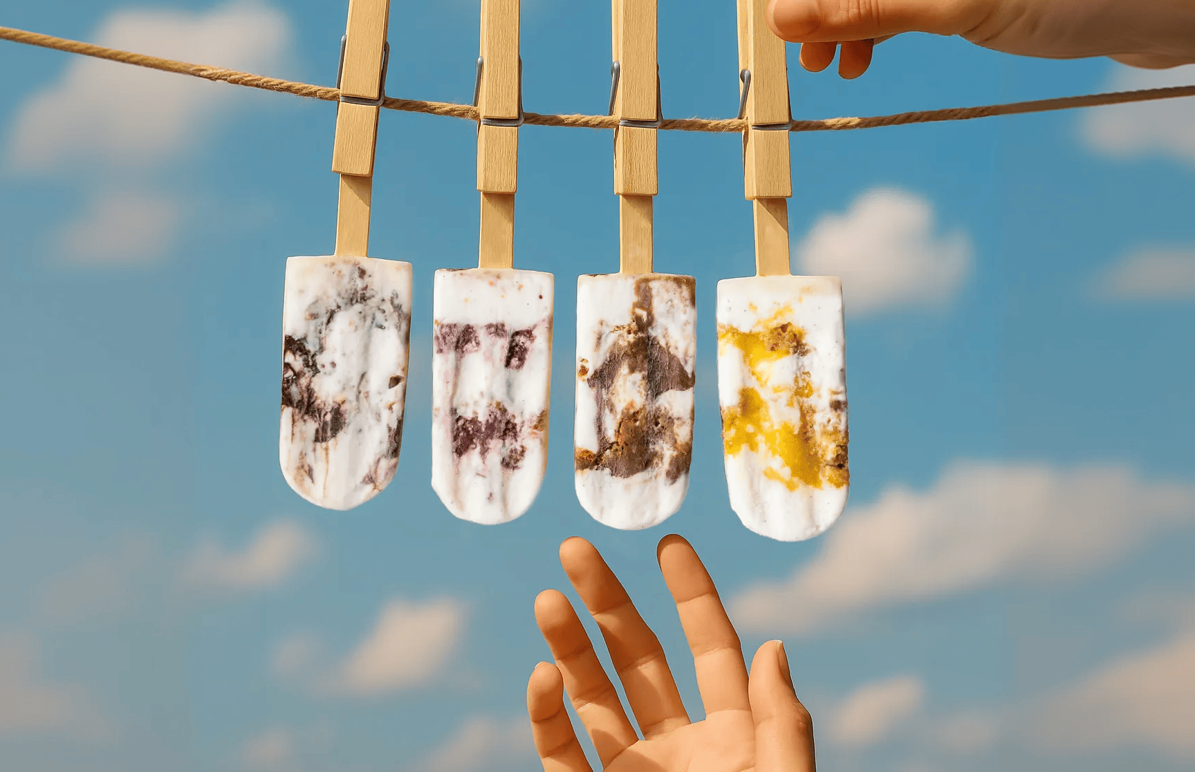 Four paletas hanging from a clothesline against a blue sky